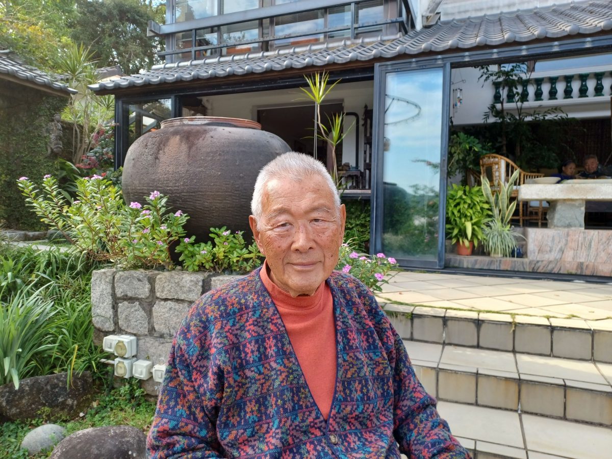 Image of James Kinoshita in front of his home with plants and a stone patio in the background.