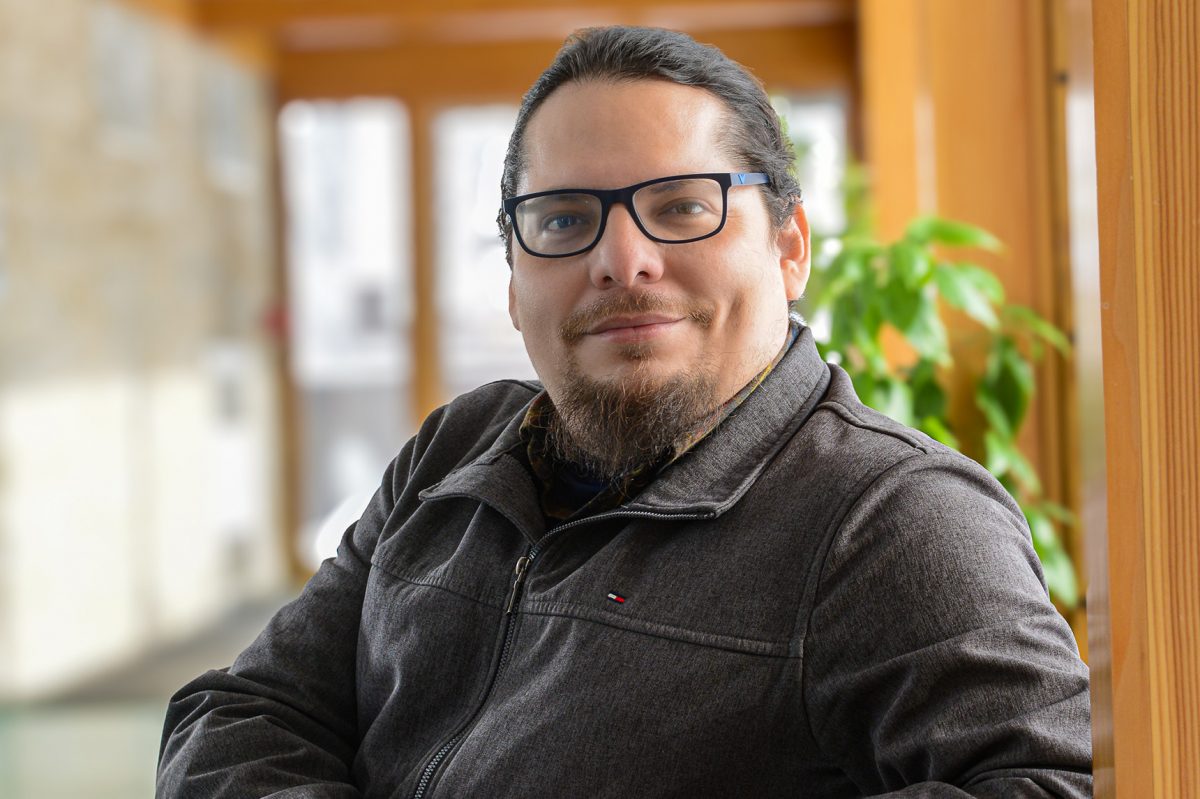 Man wearing glasses in hallway with wooden beams repeated behind him.