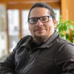 Man wearing glasses in hallway with wooden beams repeated behind him.