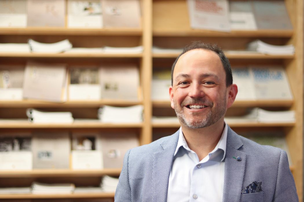 Portrait of Dr. Nathan Nickel in front of wooden shelves holding many reports.