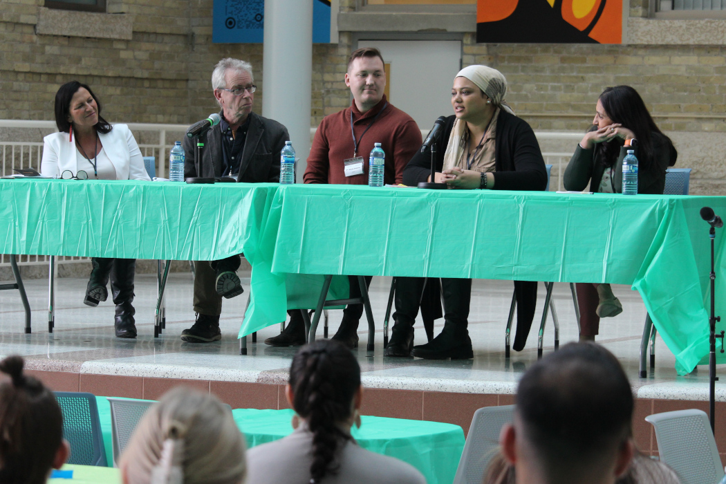 Five physicians sit behind two tables on a stage. One of them is speaking into a microphone.