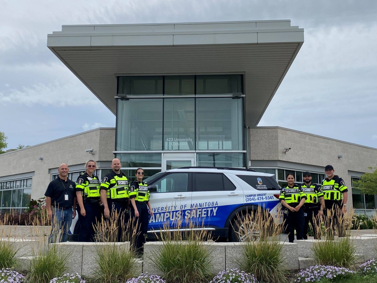 Institutional Safety Officers gathered around a Campus safety vehicle outside of a building at the Fort Garry campus