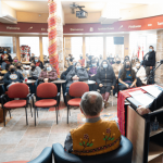 A group of UM campus community members gather indoors in chairs for a Louis Riel Day celebration.