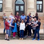 Dr. Samar Safi Harb standing in the middle of her research group smiling with students around her pointing to her in front of the UM Administration building.