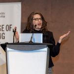 Ivy Bourgeault speaking at a podium, in front of a College of Nursing banner.