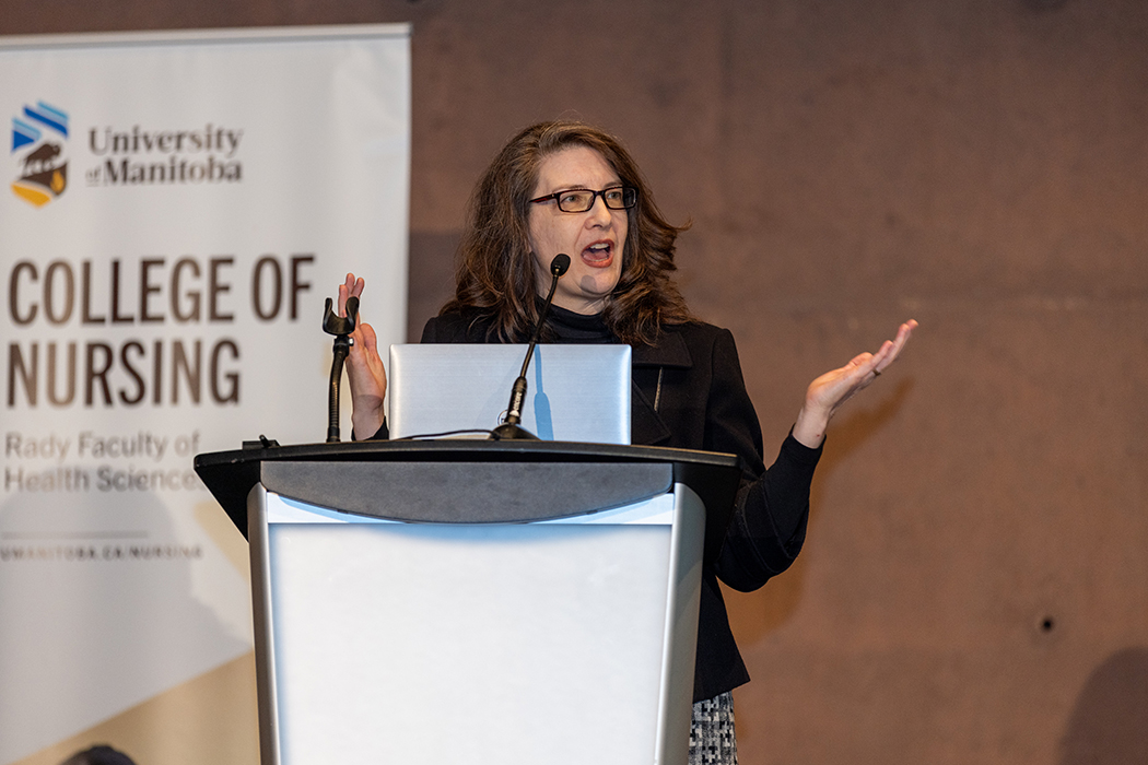 Ivy Bourgeault speaking at a podium, in front of a College of Nursing banner.
