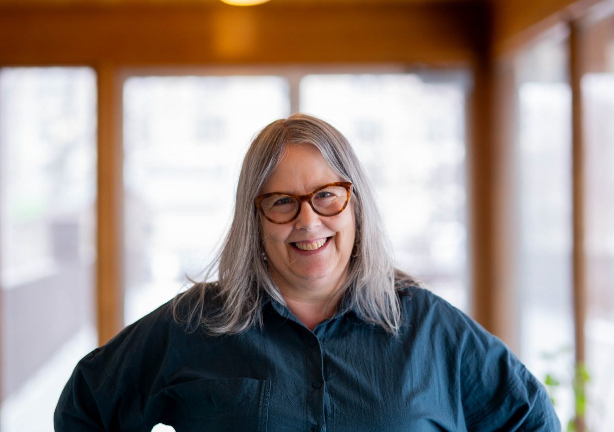Woman with shoulder length grey hair wearing brown rimmed glasses - big smile
