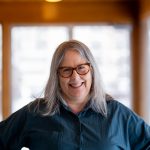 Woman with shoulder length grey hair wearing brown rimmed glasses - big smile