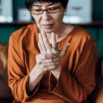 A woman rubs her hands and looks distressed, as if they are sore.