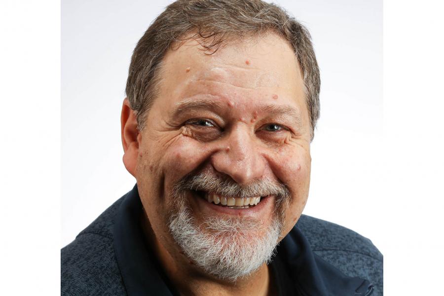 Man with short brown hair, grey short beard, big smile and a dark blue collared shirt.