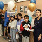 Eight kids pose for the photo holding helium-filled balloons. A dental student stands with them.
