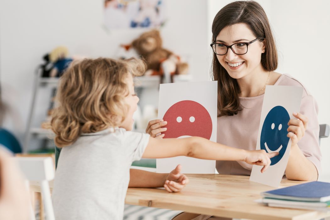 A woman shows images of smiling and frowning faces to a young girl.