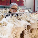 female with short grey hair overlooking a rack of unique shaped felt fabric jewlery