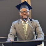 Photo of student in cap and suit at podium