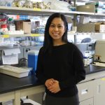 Dr. Janilyn Arsenio leans against a counter in her lab. Items used for scientific research sit on shelves behind her and on the counter.