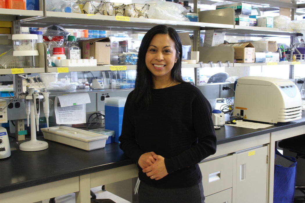 Dr. Janilyn Arsenio leans against a counter in her lab. Items used for scientific research sit on shelves behind her and on the counter.