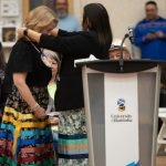 A woman in a ribbon skirt is presented with a beaded medallion.