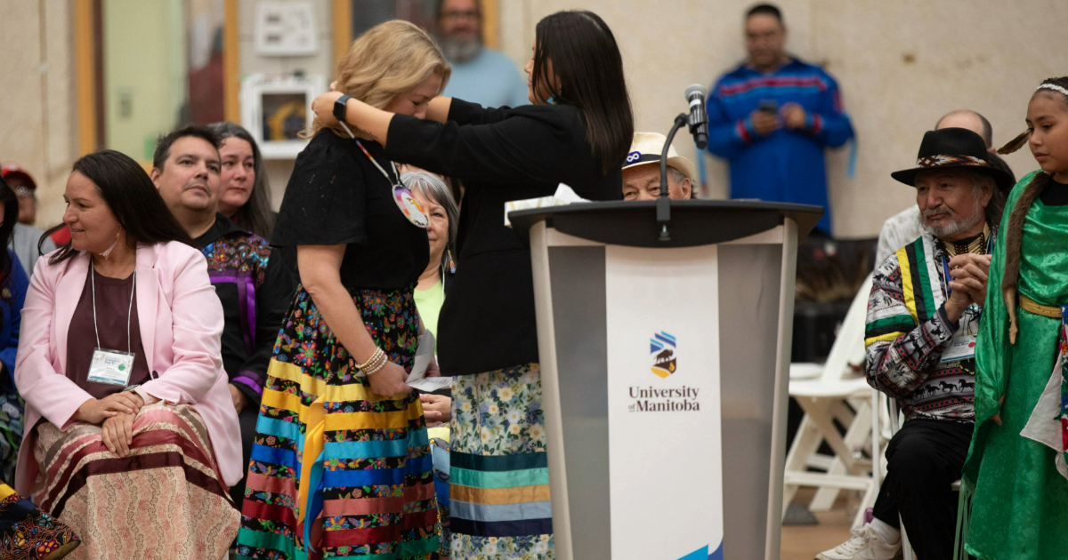 A woman in a ribbon skirt is presented with a beaded medallion.