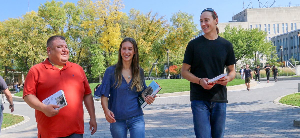 Two men and a woman walk across the UM campus.