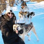 Student crouches in the snow to pet a dog.