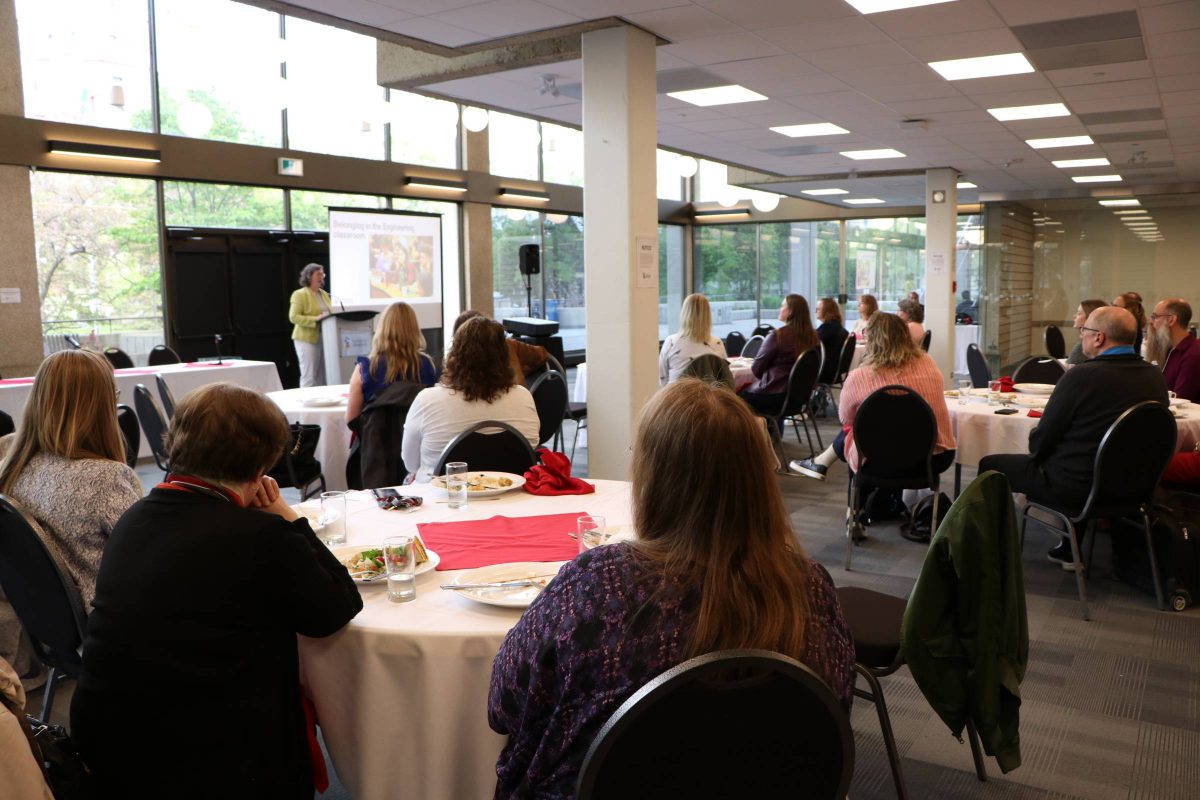 People sitting around tables watching a person at a pedestal present.