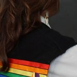 An Indigenous student with long hair poses with their back to the camera, only shoulders visible, wearing a black ribbon vest with a white t-shirt.