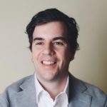 Headshot of new assistant professor Kenneth Grad wearing a white shirt and grey blazer smiling and looking left of camera.