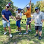 Four people posing with golf clubs on a golfcourse.