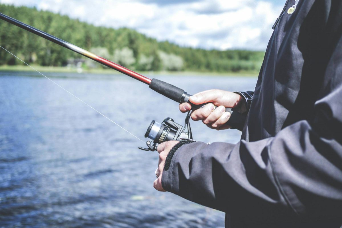 Person holding a fishing road standing near water.