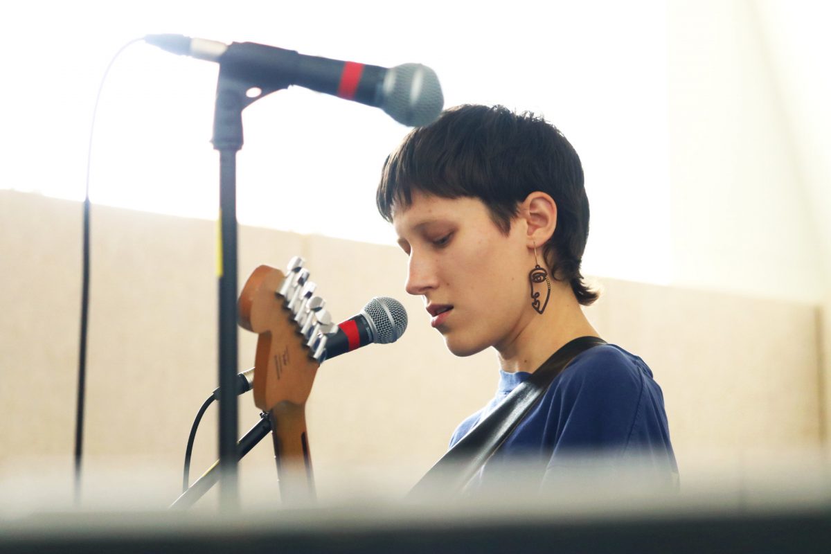 Person with large earrings is about to sing into a microphone - they are holding a guitar