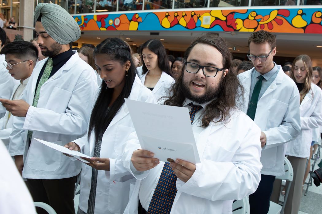Students wearing white coats stand while reciting the Physician's Pledge.