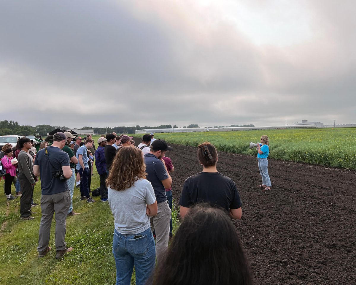 People gather around a speaker on the edge of a tilled field