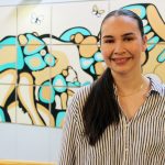 Justice Spence stands in the College of Nursing atrium with a colourful mural behind her.