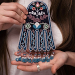 Woman with brown hair holds a beaded artwork.