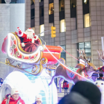 Santa Claus in a sleigh pulled by reindeer. In the background, trees bedecked with Christmas lights and skyscrapers.