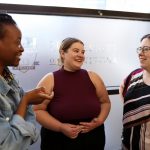 Three women stand in a semi-circle having a conversation.