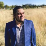 Kyle Bobiwash stands in a field, wearing a blue suit and looking off to the side