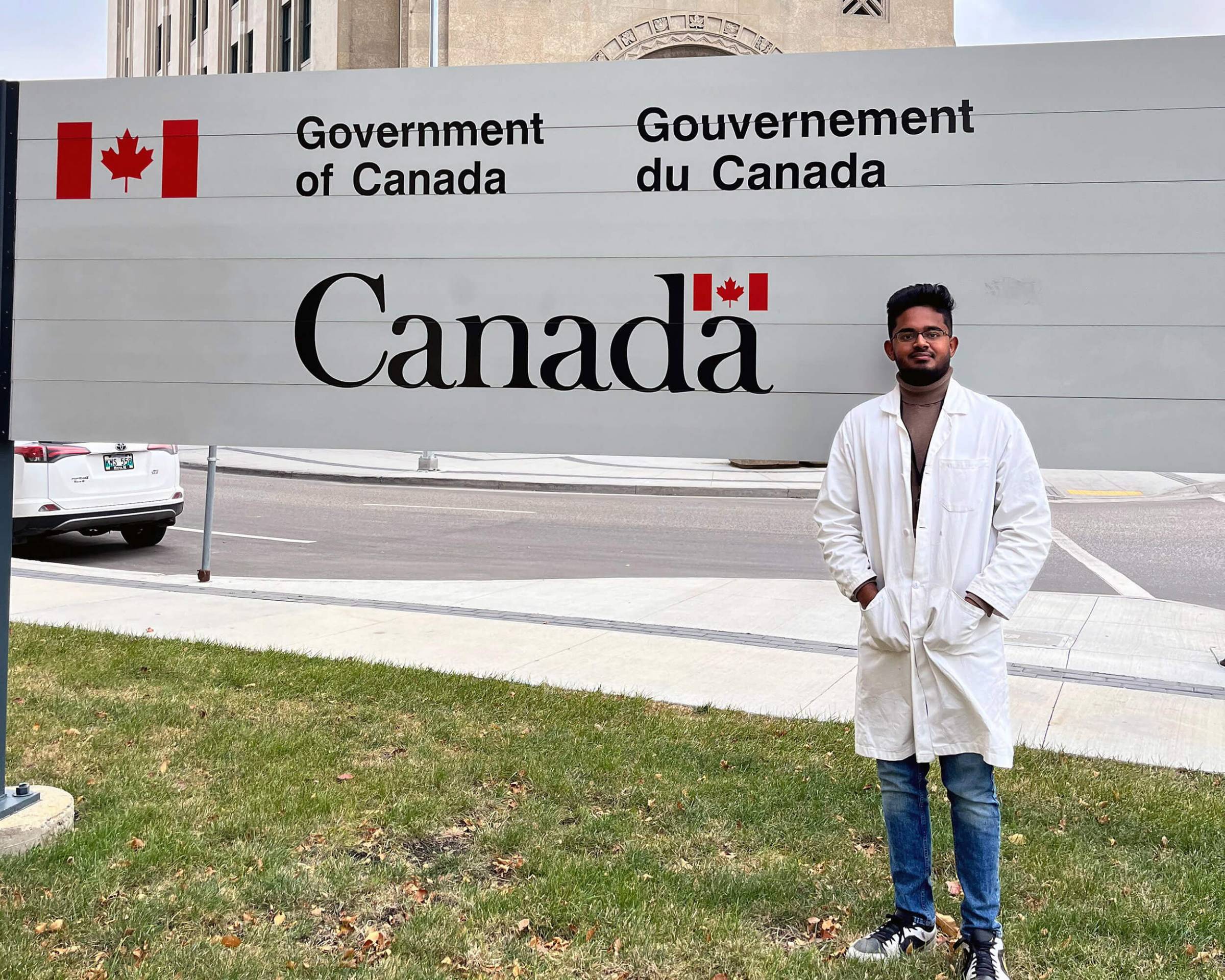 Akshai Arulmani Sukaraj stand in front of a GOM sign