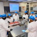 Students gather around a steel table to learn about meat inspection