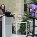 Dr. Nicole Harder stands at a podium. A TV screen shows nursing students wearing VR headsets.