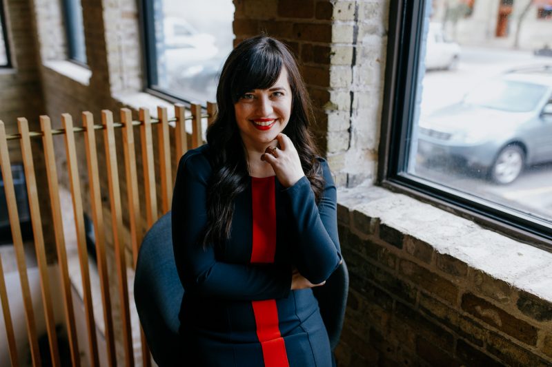 Photo of Elise Epp a smiling woman with long dark hair wearing a blue and red knit dress.