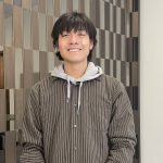 Student in brown hoodie standing in front of a checkered wall.