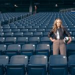 Christina Litz faces the camera, standing in the seats of the stadium