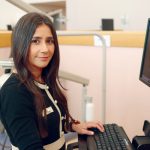 Dr. Julie Pfeffer stands at a computer in a dental clinic. An X-ray of teeth is on the computer screen.