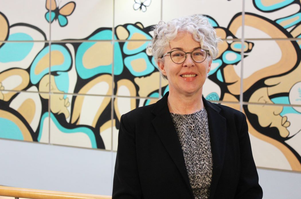 Kellie Thiessen stands in front of a mural at the College of Nursing.