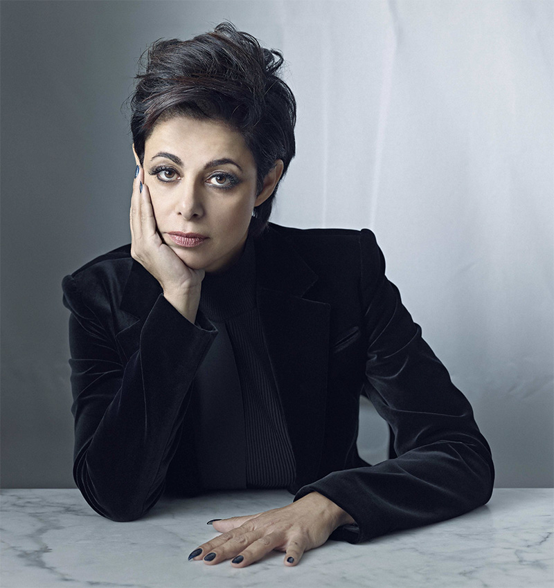 Photo of famous Toronto Criminal defence lawyer Marie Henein leaning on one elbow with her face in one hand, looking piecingly at the camera. She wears all black with one hand pressed on the table in front of her. Her face is expressionless.
