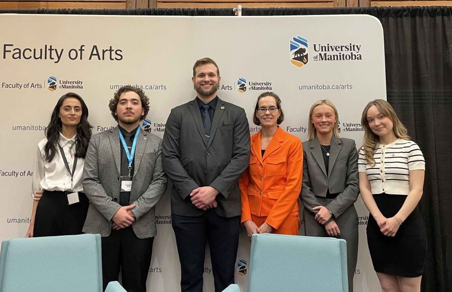 Group of six people standing in front of a banner, all with their hands crossed in front of their bodies.