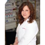 Portrait of Alia Marcinkow in a pharmacy. She is wearing a white pharmacist's coat.
