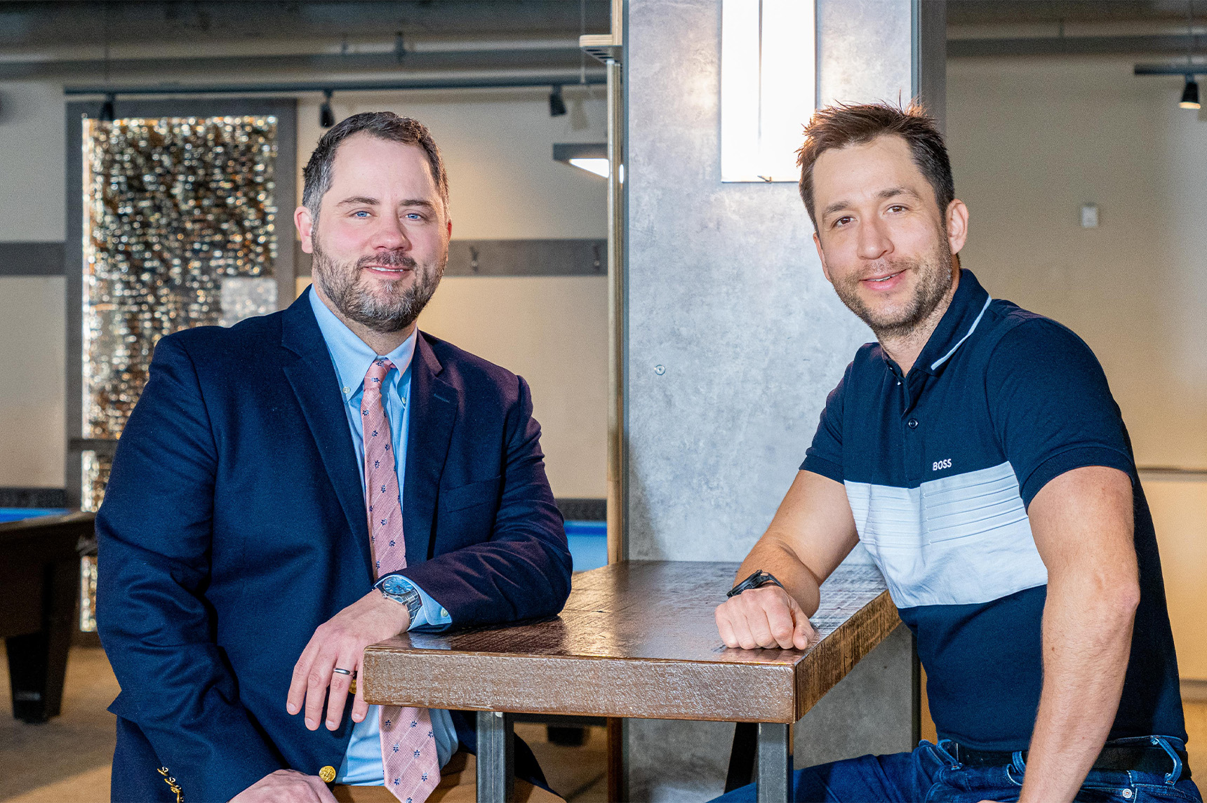 Two men sitting at a restaurant table, looking into the camera and smiling.