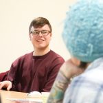 Student talking with another student on a rounded table while smiling.